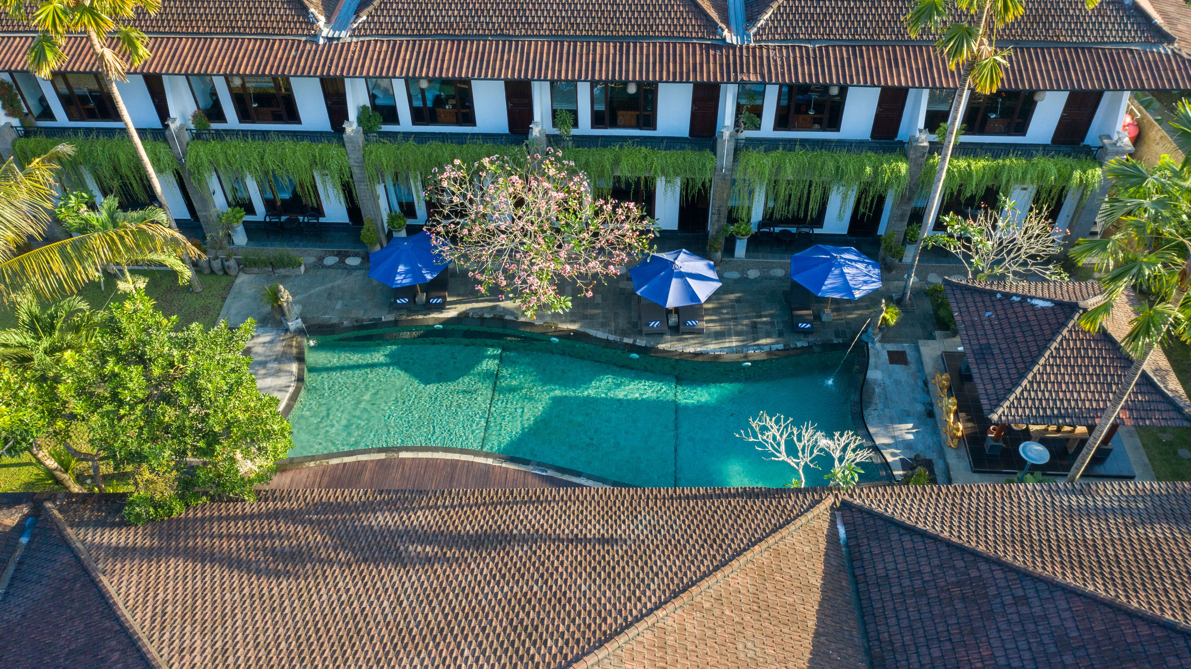 An aerial view of a resort with a swimming pool, palm trees, and a building with a tiled roof.