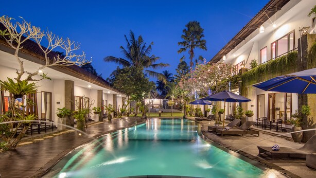 A pool area with lounge chairs and umbrellas, surrounded by buildings with outdoor seating and plants. - Ubud Raya Boutique Hotel (Ubud)