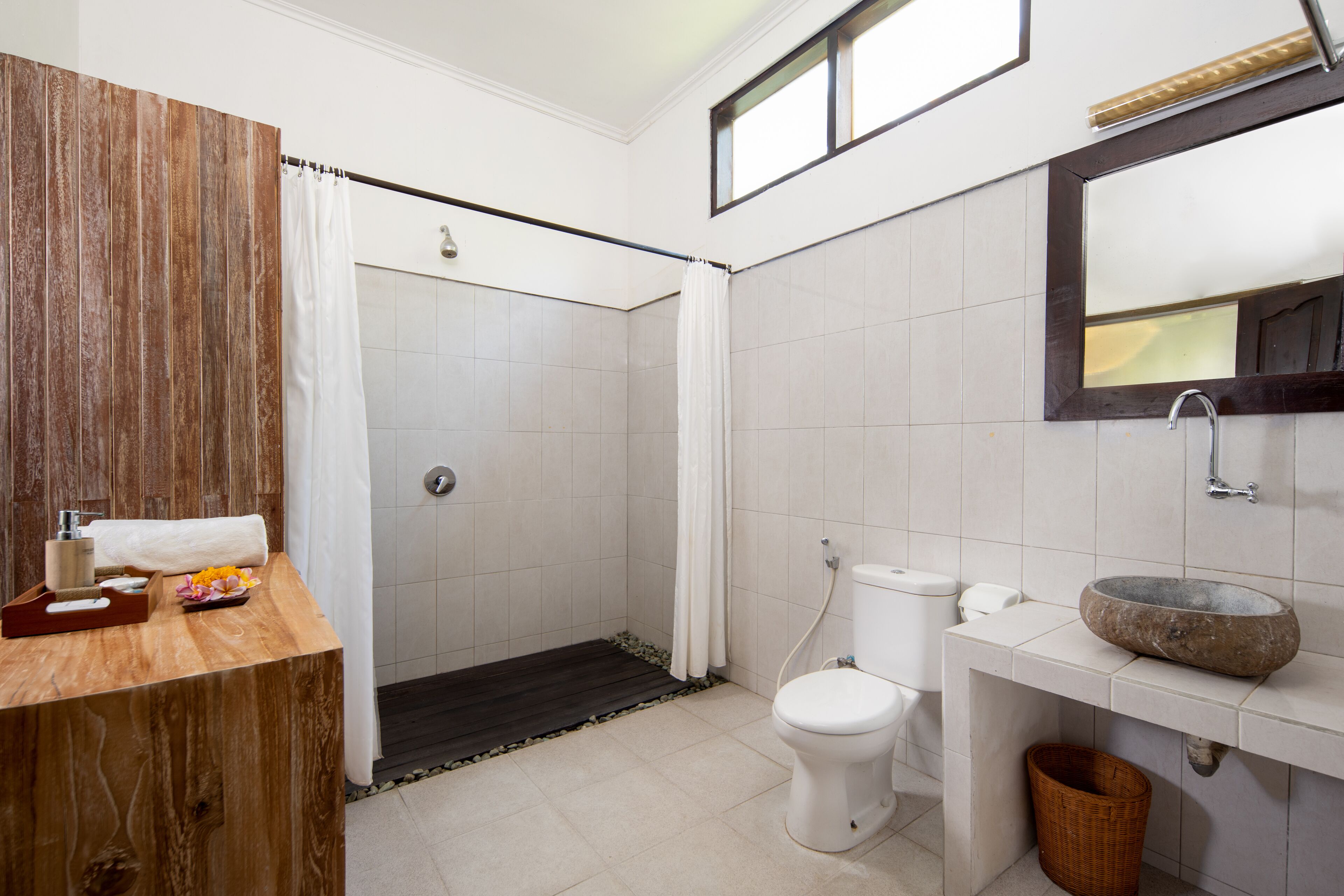 A bathroom with a wooden vanity, a white toilet, a stone sink, and a shower area.