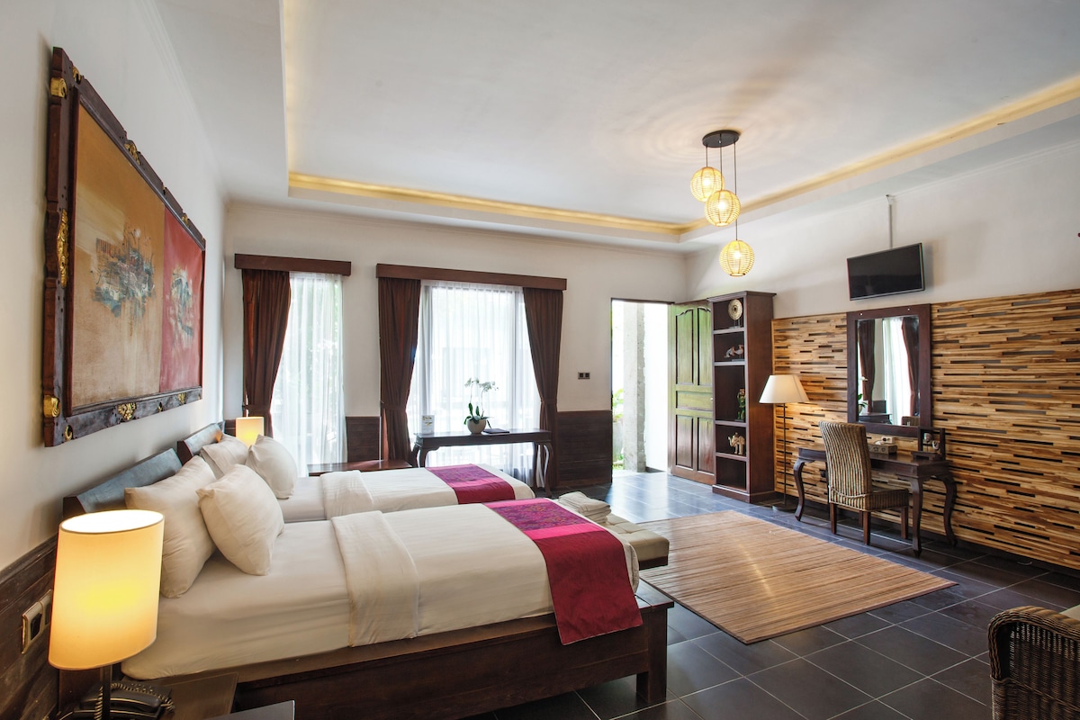 A hotel room with a bed, bedside lamps, a painting, a desk, a chair, and a television.