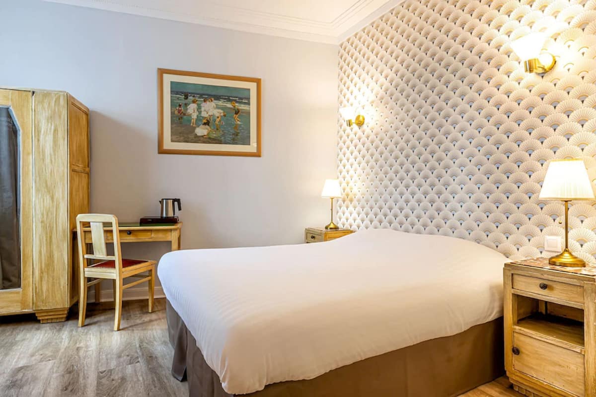 A hotel room with a large bed, a wooden desk, a chair, a wardrobe, and a wall with a textured pattern.