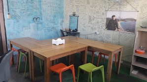 Une pièce avec une table en bois, des chaises colorées, un miroir et un mur recouvert d’inscriptions.