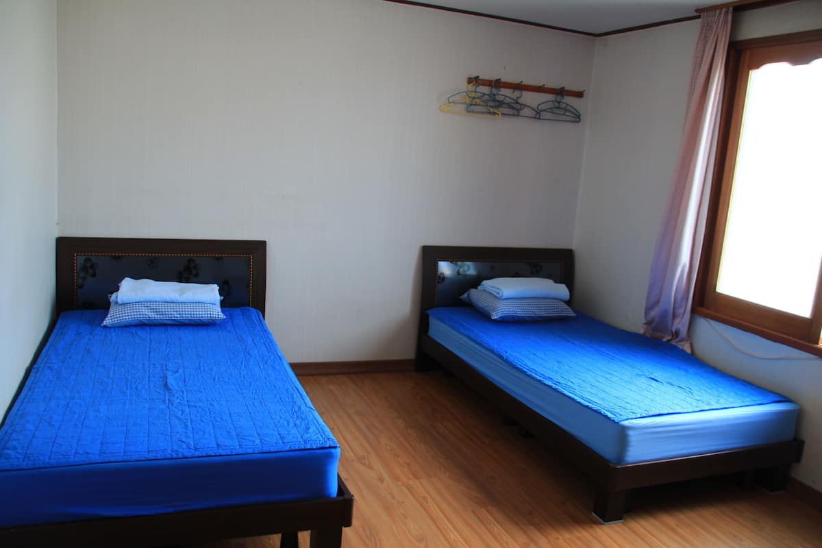 A room with two single beds, wooden flooring, a window with curtains, and a wall-mounted coat rack.