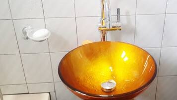 A bathroom with a glass bowl sink, a green pedestal, and a white tiled wall.