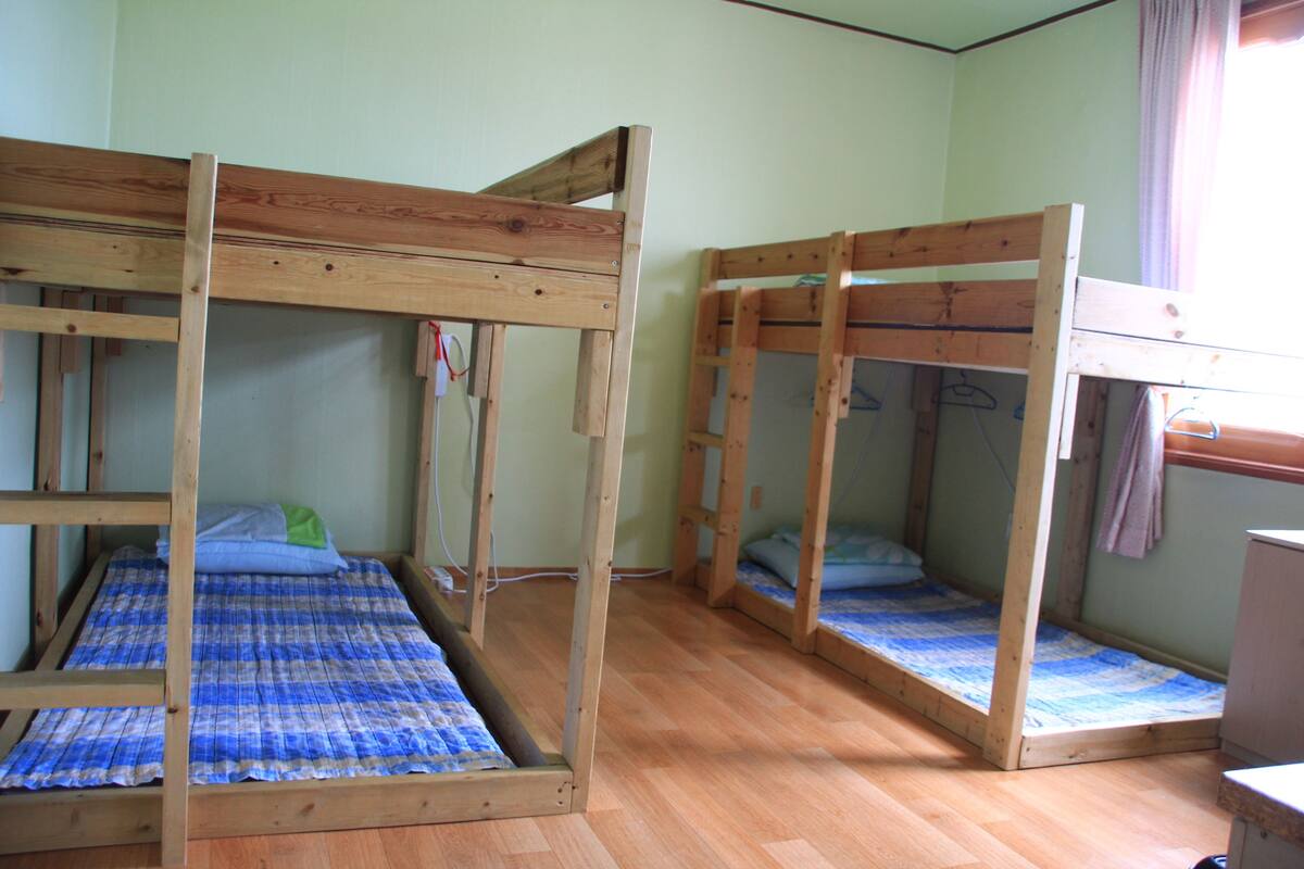 A room with three bunk beds, wooden flooring, and a window with curtains.