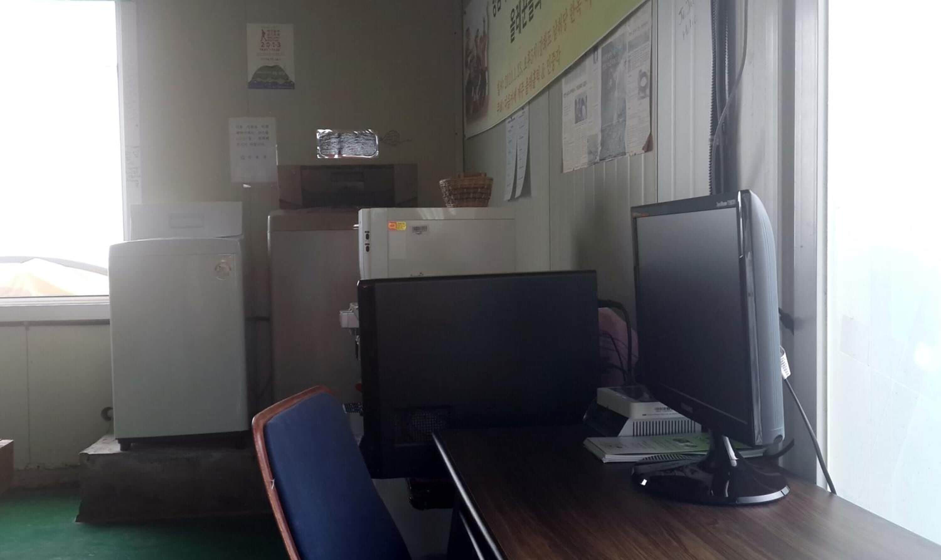 Un petit bureau équipé de deux écrans d’ordinateur, d’un réfrigérateur et d’un distributeur d’eau.