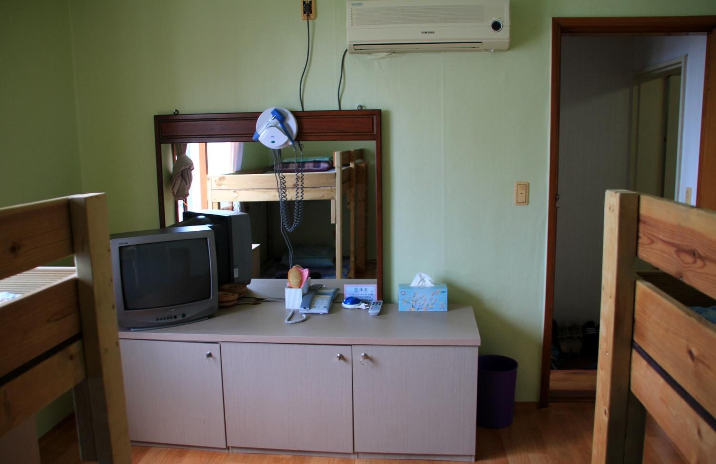 Een kleine kamer met een houten kast, een televisie, een spiegel en een luchtverwarmer aan de muur.