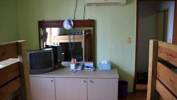 Een kleine kamer met een houten kast, een televisie, een spiegel en een luchtverwarmer aan de muur.