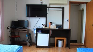 Une chambre avec un lit, un bureau avec un ordinateur, un petit réfrigérateur et un téléviseur fixé au mur.