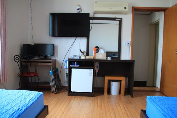 Un dormitorio con una cama, un escritorio con computadora, un refrigerador pequeño y un televisor montado en la pared.