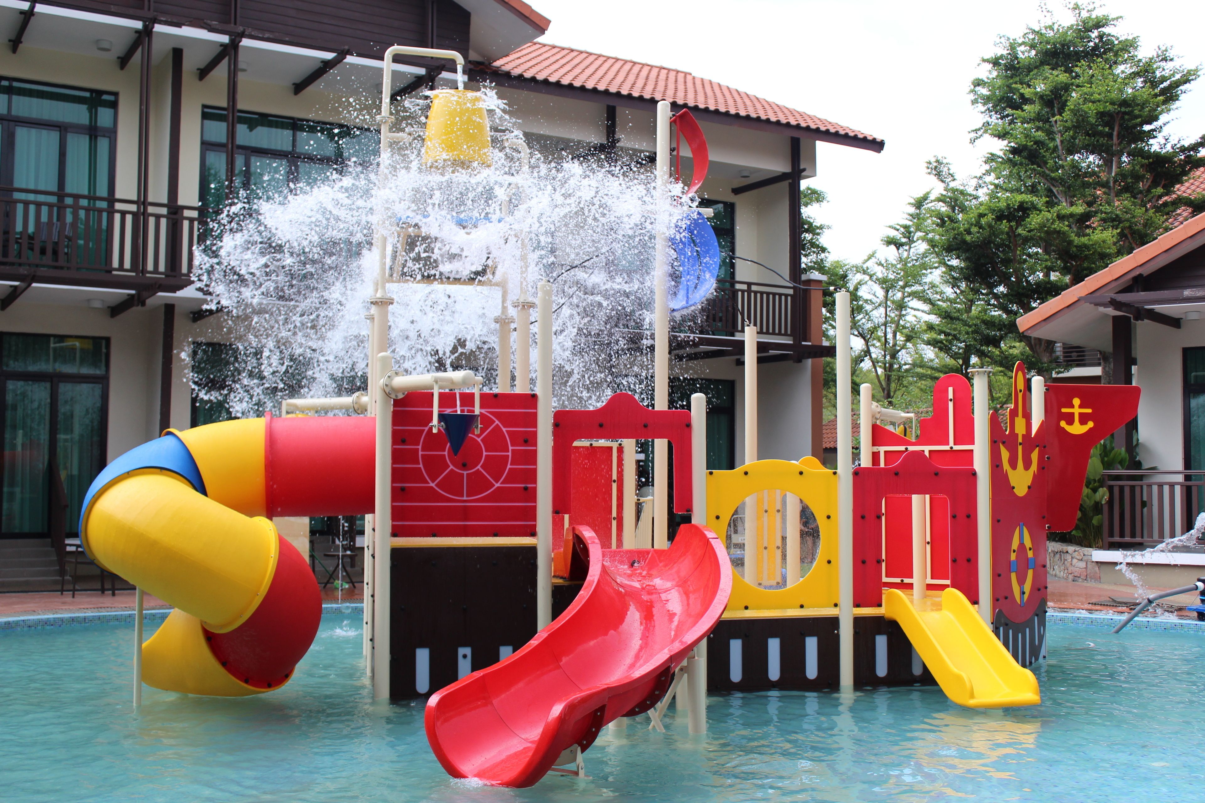 A water play area with slides and water jets, surrounded by a building with balconies and windows.