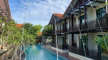 Relax by the serene pool surrounded by lush greenery and two-story buildings with balconies offering a view of the pool and surrounding landscape.
