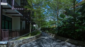 A pathway flanked by lush greenery and a building with a balcony. - Espira Kinrara (Puchong)