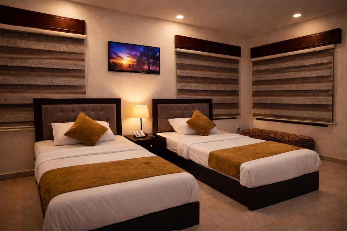 A hotel room with two beds, a nightstand with a lamp, and a painting on the wall.