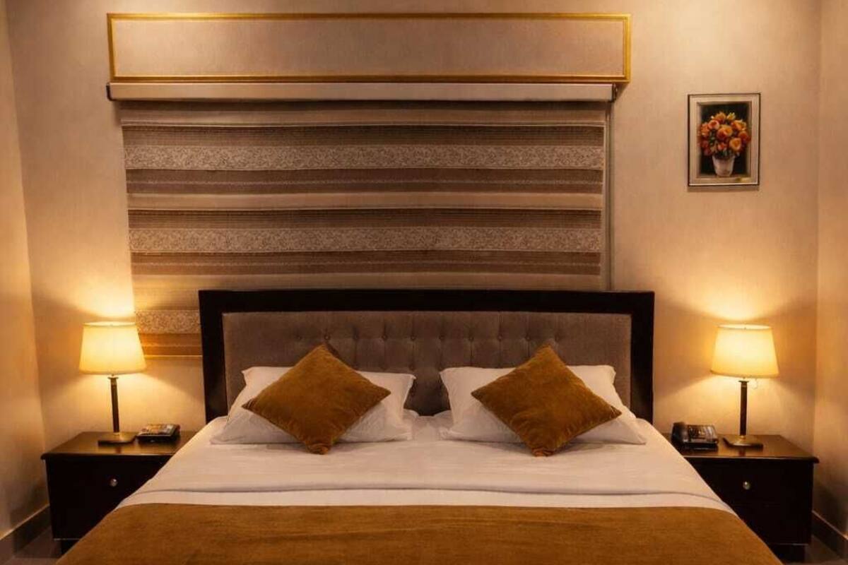 A hotel room with a large bed, two bedside tables with lamps, a headboard with horizontal stripes, and a framed picture on the wall.