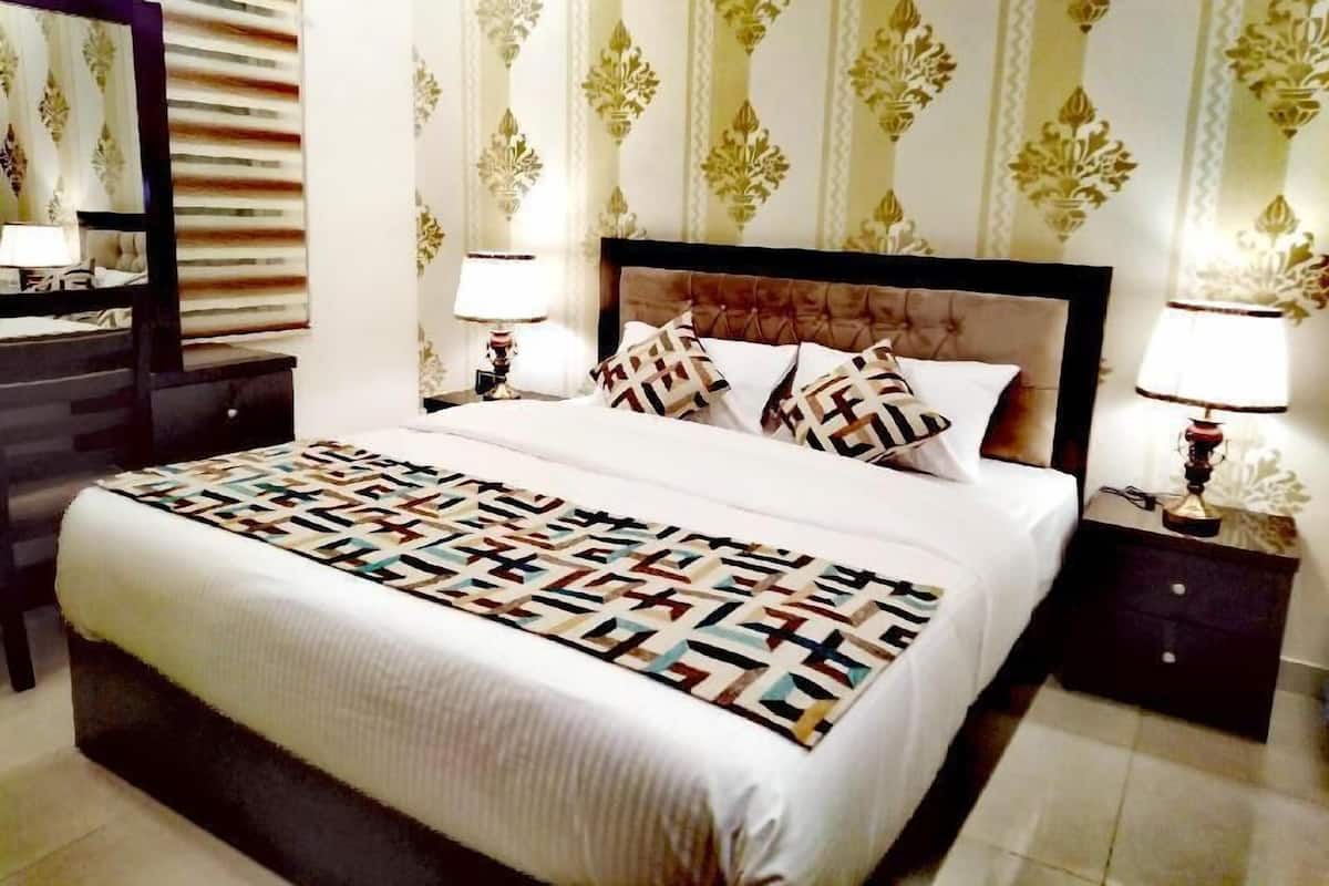A hotel room with a large bed, two bedside tables with lamps, a dresser, and patterned wallpaper.