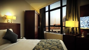 Habitación de hotel con cama, mesita de noche, lámpara, televisor y ventana con vista a un edificio y una torre.