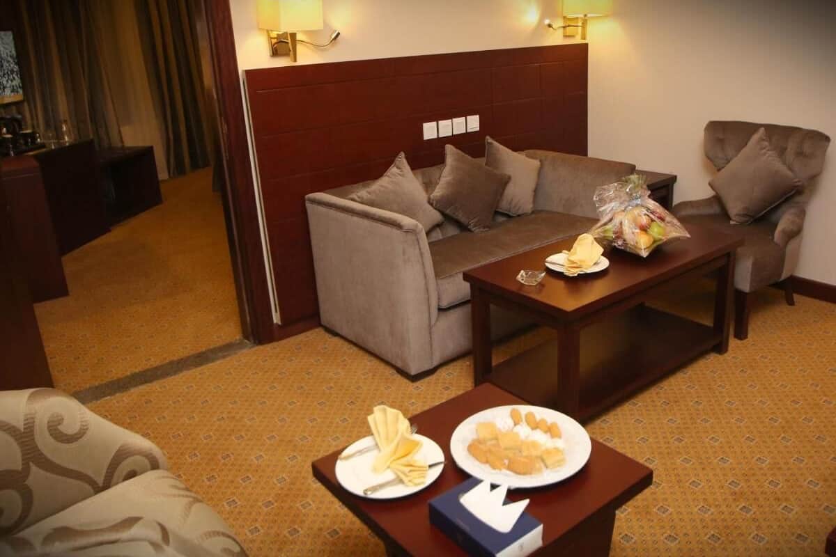 Een hotelkamer met een sofa, een bijzettafeltje met ontbijtartikelen en een bed met hoofdeinde.