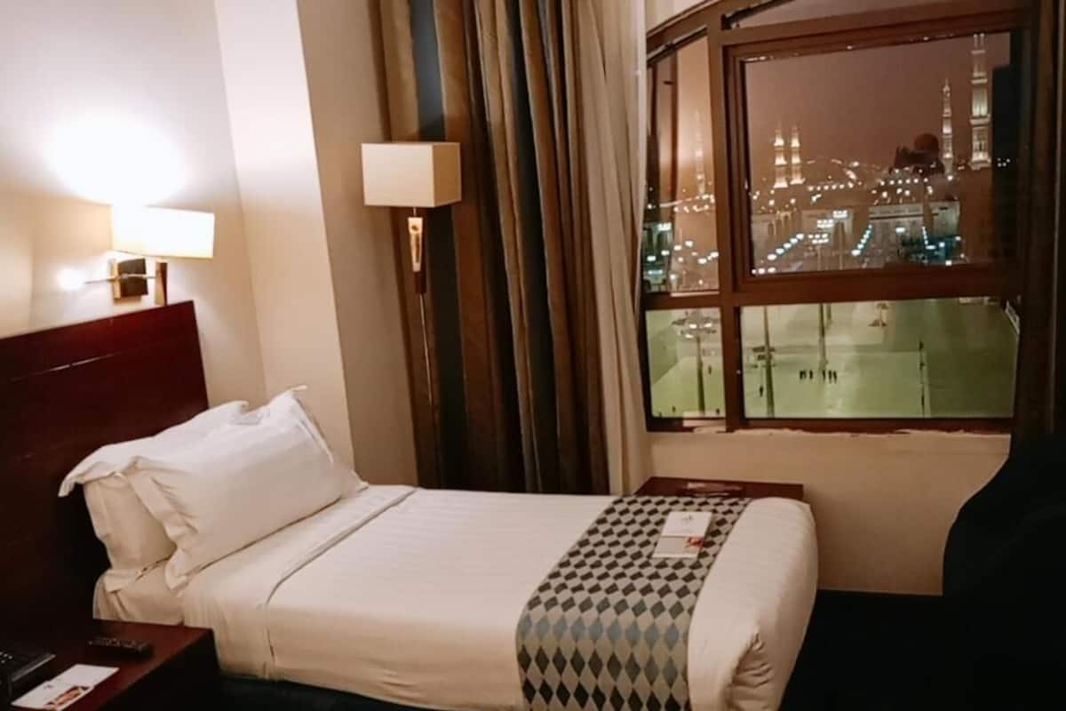 Een hotelkamer met een bed, nachtkastje, lamp en raam met uitzicht op een stadsbeeld 's nachts.