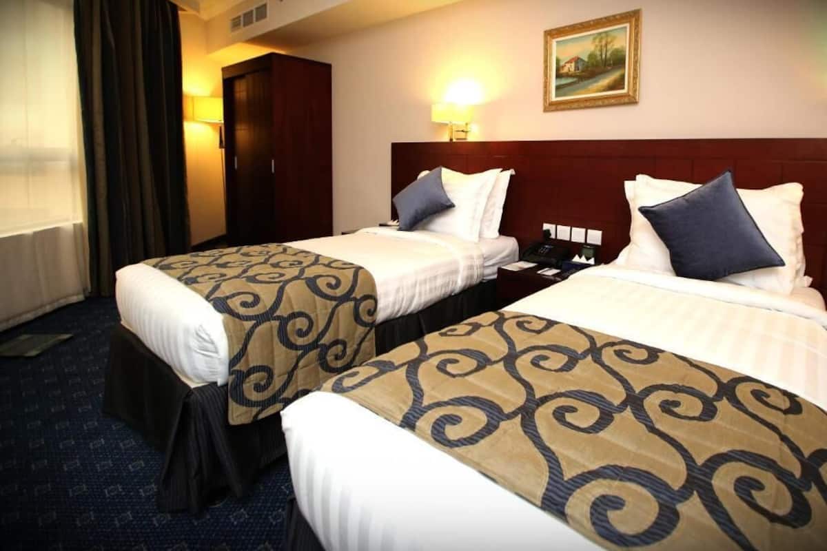 Hotelkamer met twee bedden, elk voorzien van een beddekleed met patroon, een nachtkastje, een lamp en een schilderij aan de muur.