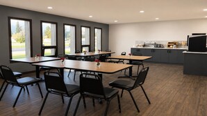 A modern dining area with multiple tables and chairs, a kitchen area with appliances, and large windows offering views of the outdoors. - SureStay by Best Western Smithers (Smithers)