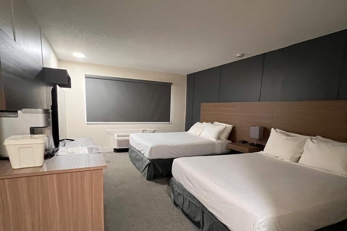 A hotel room with two beds, a desk, a chair, a lamp, and a window with blinds.