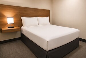 Una habitación de hotel con una cama, una mesita de noche con lámpara y un cabecero de madera.