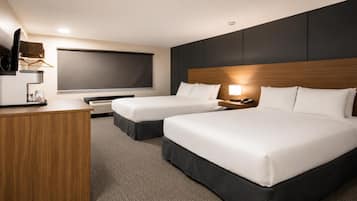 A hotel room with two beds, a desk, a flat-screen TV, and a bedside lamp.