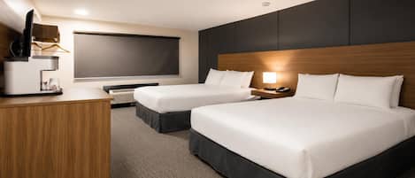 A hotel room with two beds, a desk, a flat-screen TV, and a bedside lamp.