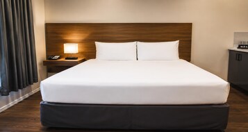 Una habitación de hotel con una cama grande, una mesita de noche con una lámpara y un teléfono.