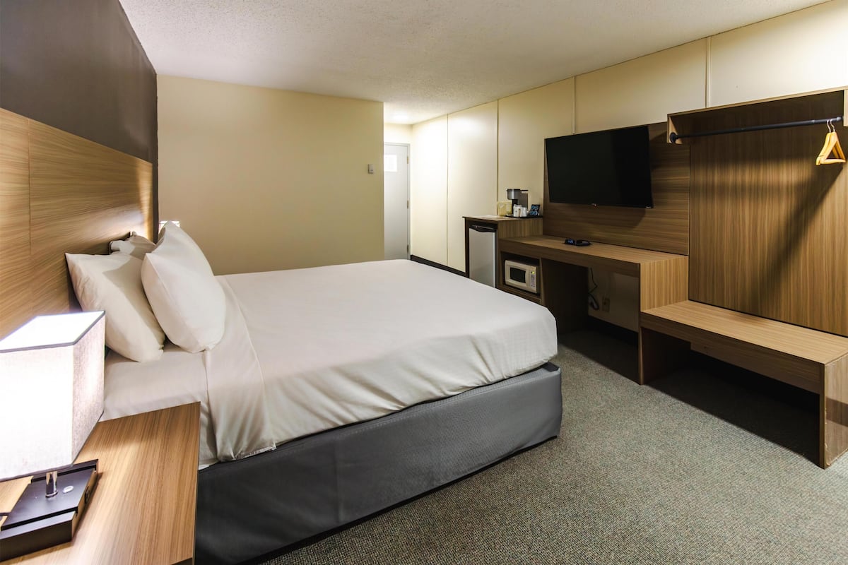 A hotel room with a bed, a desk with a flat-screen TV, a microwave, and a small seating area.