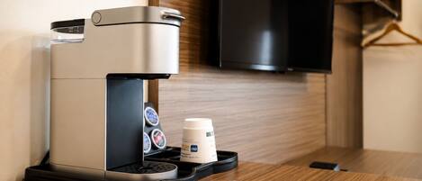 A coffee machine with a milk frother and a disposable cup on a wooden table in a hotel room.