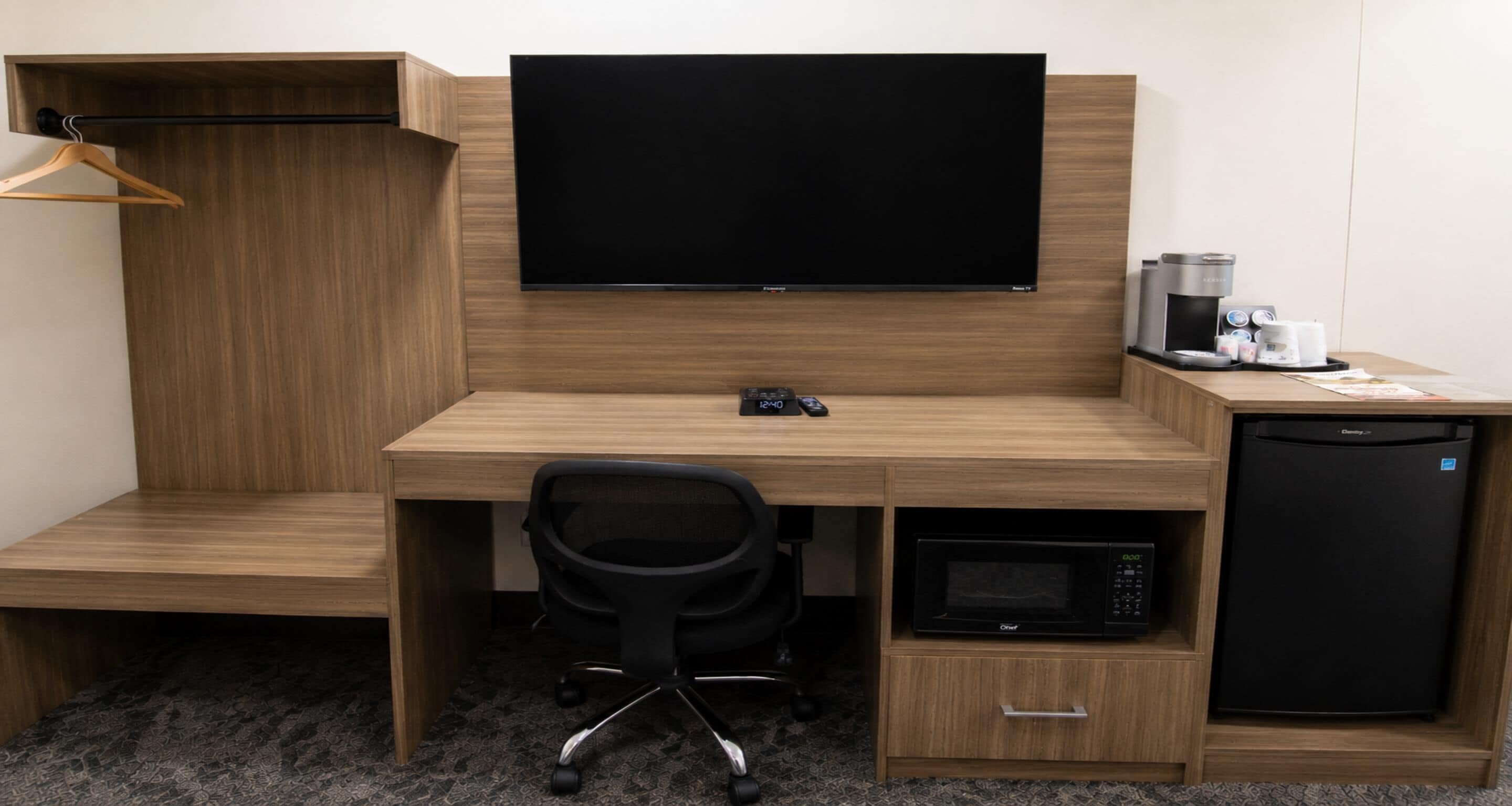 Une chambre d’hôtel équipée d’un bureau en bois, d’un téléviseur à écran plat, d’une machine à café, d’un four à micro-ondes et d’un mini-réfrigérateur.