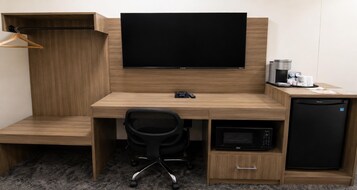 A hotel room with a wooden desk, a flat-screen TV, a coffee maker, a microwave, and a mini fridge.