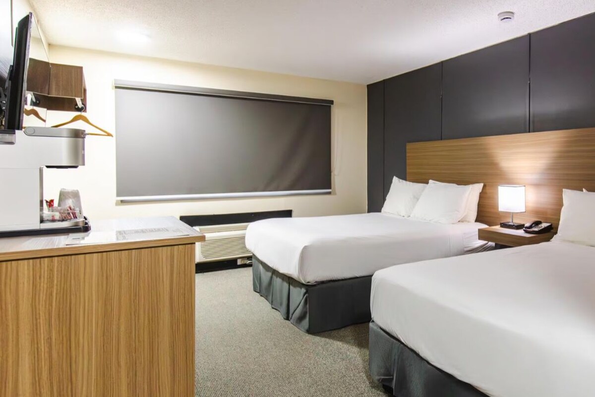 A hotel room with two beds, a desk, a TV, and a window.