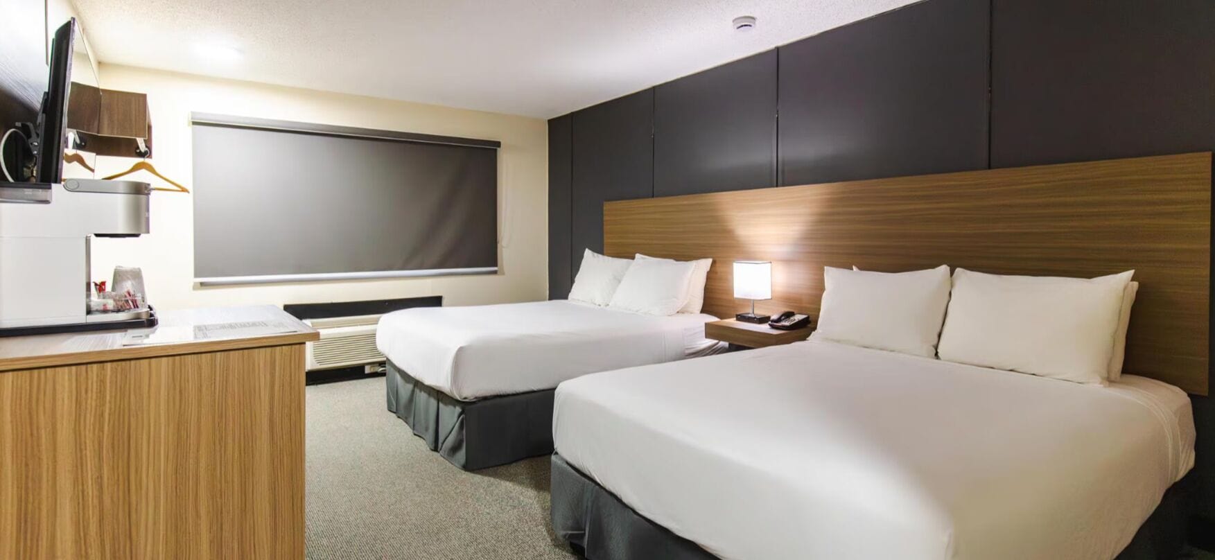 A hotel room with two beds, a desk, a TV, and a window.