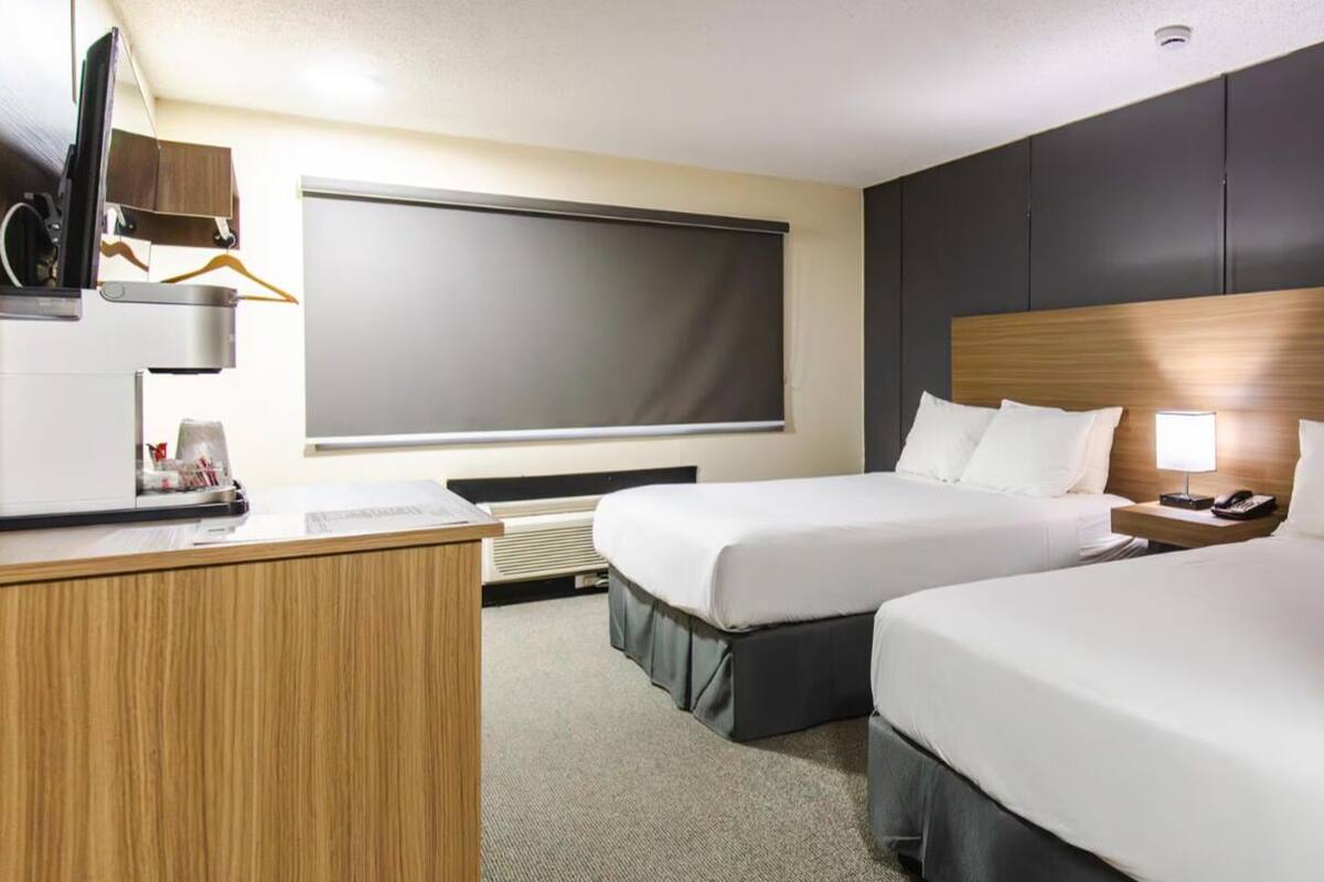 A hotel room with two beds, a desk, a TV, and a window.