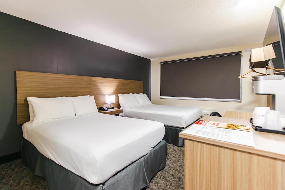 A hotel room with two beds, a desk, a lamp, and a window.