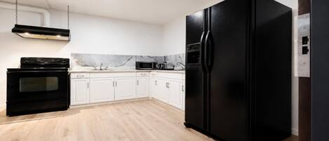 Una cocina con armarios blancos, un refrigerador negro, una estufa y un microondas.