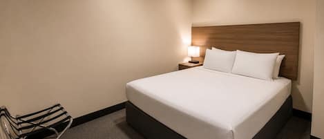 A hotel room with a large bed, a nightstand with a lamp, and a chair.