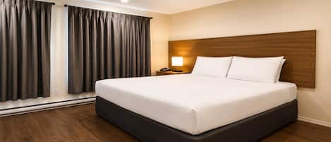 A hotel room with a large bed, wooden headboard, a bedside table with a lamp, and a window with curtains.
