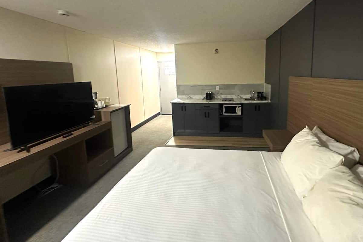 A hotel room with a bed, a TV, a small kitchenette, and a desk.
