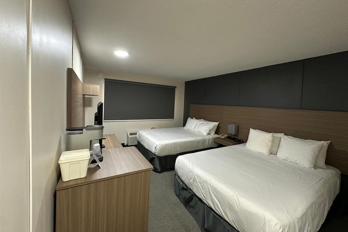 A hotel room with two beds, a desk with a telephone, a mirror, and a large window.