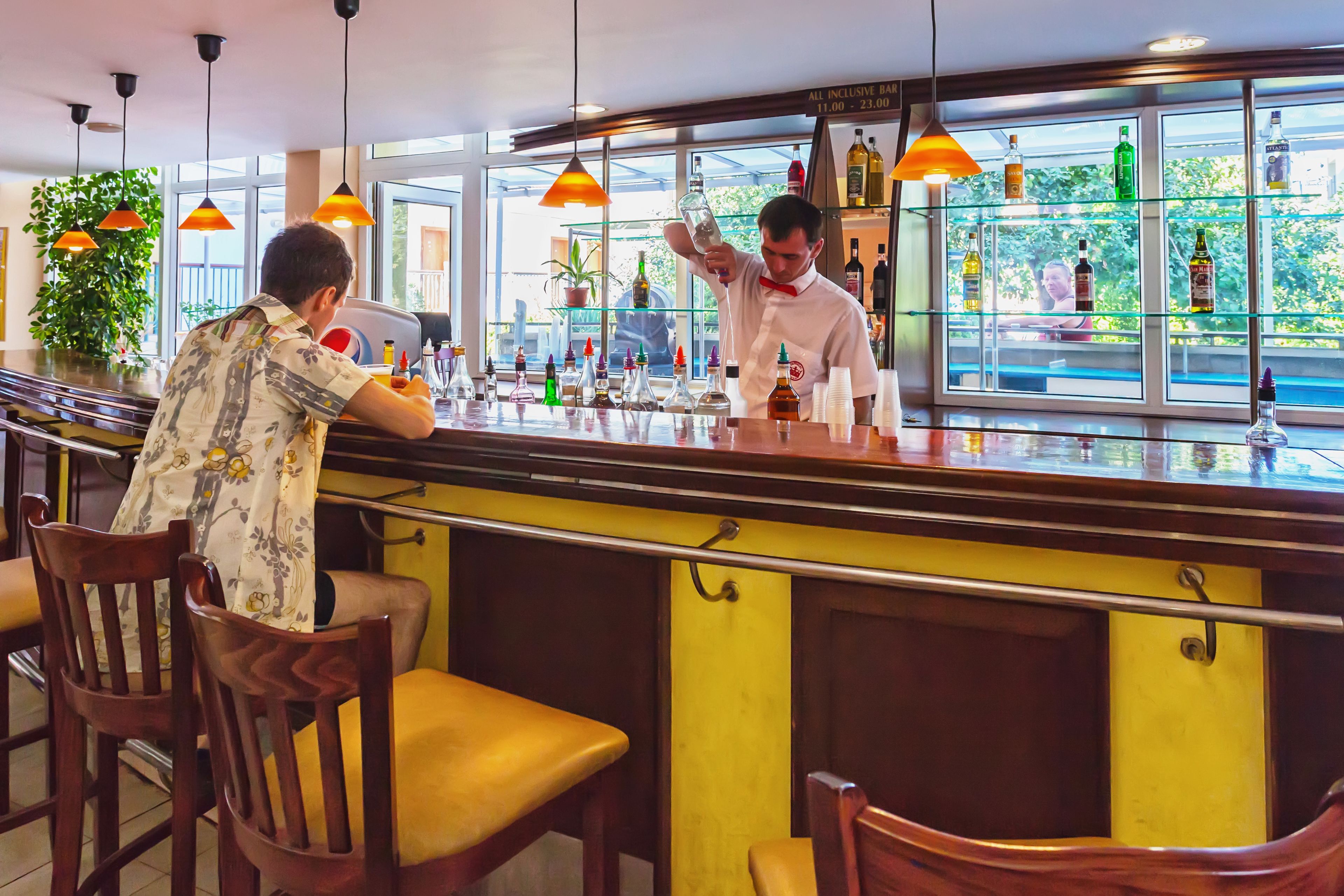 A bar area with wooden chairs, a bartender, and shelves of liquor bottles.