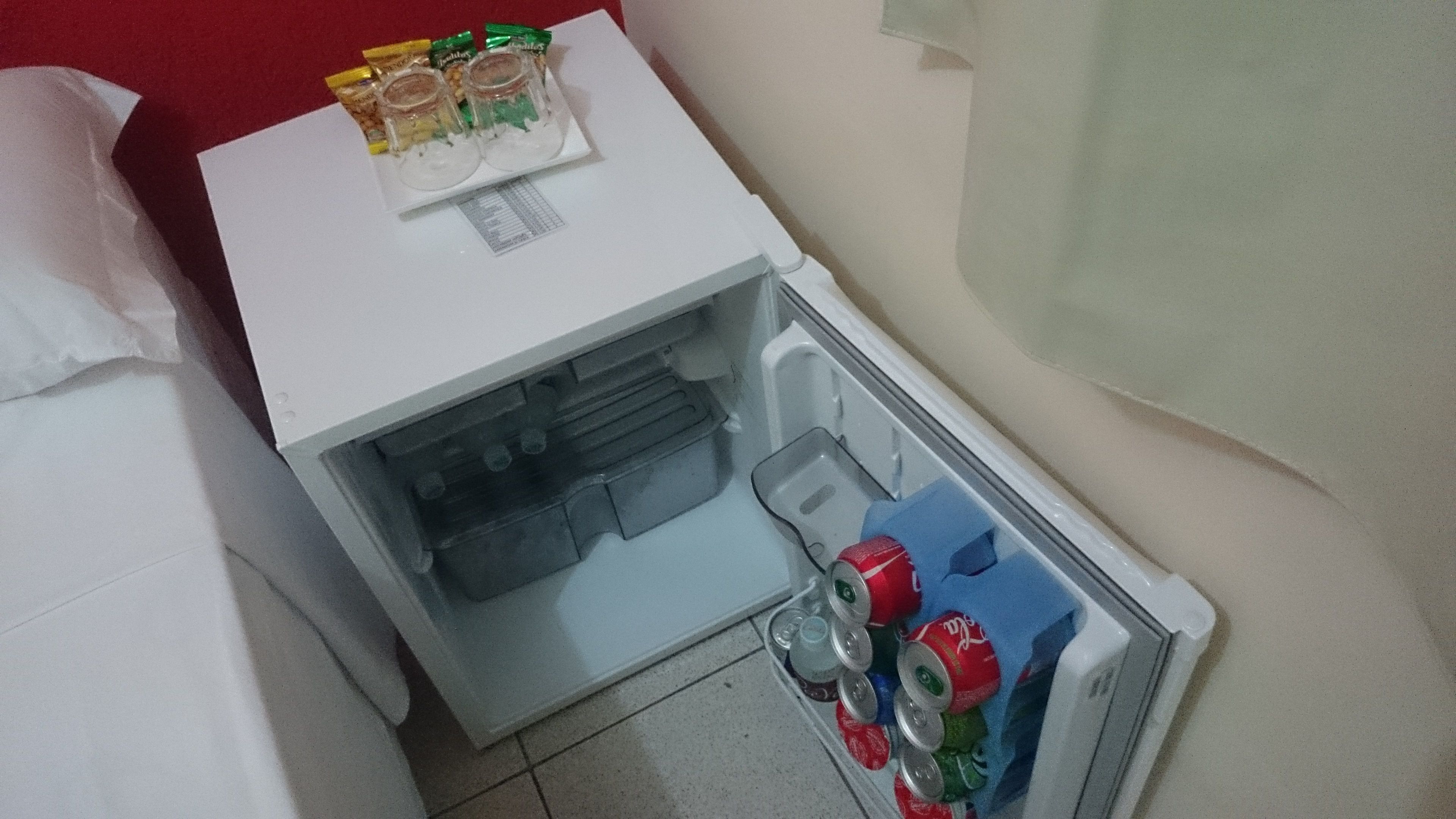 Un petit réfrigérateur à l’intérieur blanc, contenant quelques bouteilles et quelques canettes.