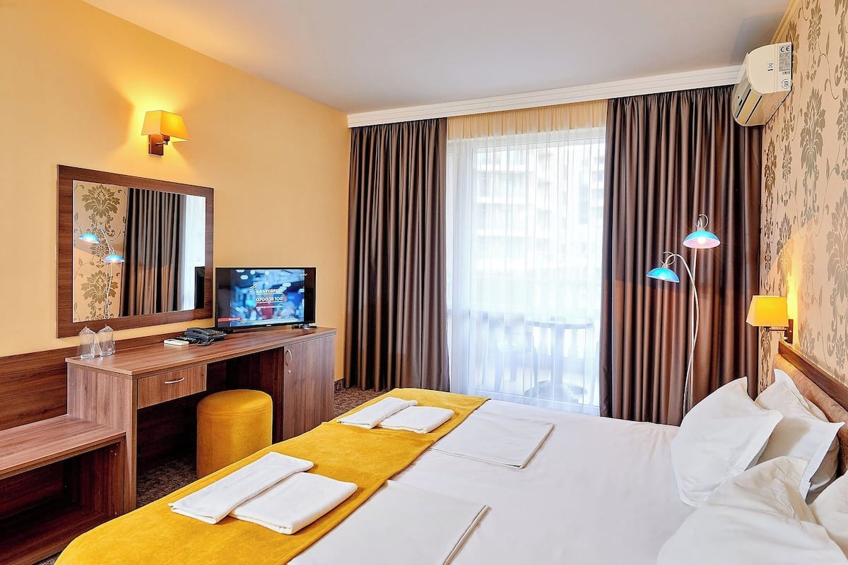 A hotel room with a bed, a desk, a television, and a window with curtains.