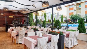 Un restaurante al aire libre con mesas, sillas, un bar y una piscina al fondo.
