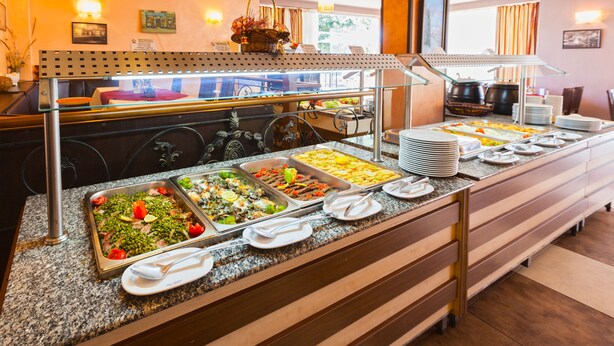 Un bufé con diversos alimentos y un área de comedor con mesas y sillas.