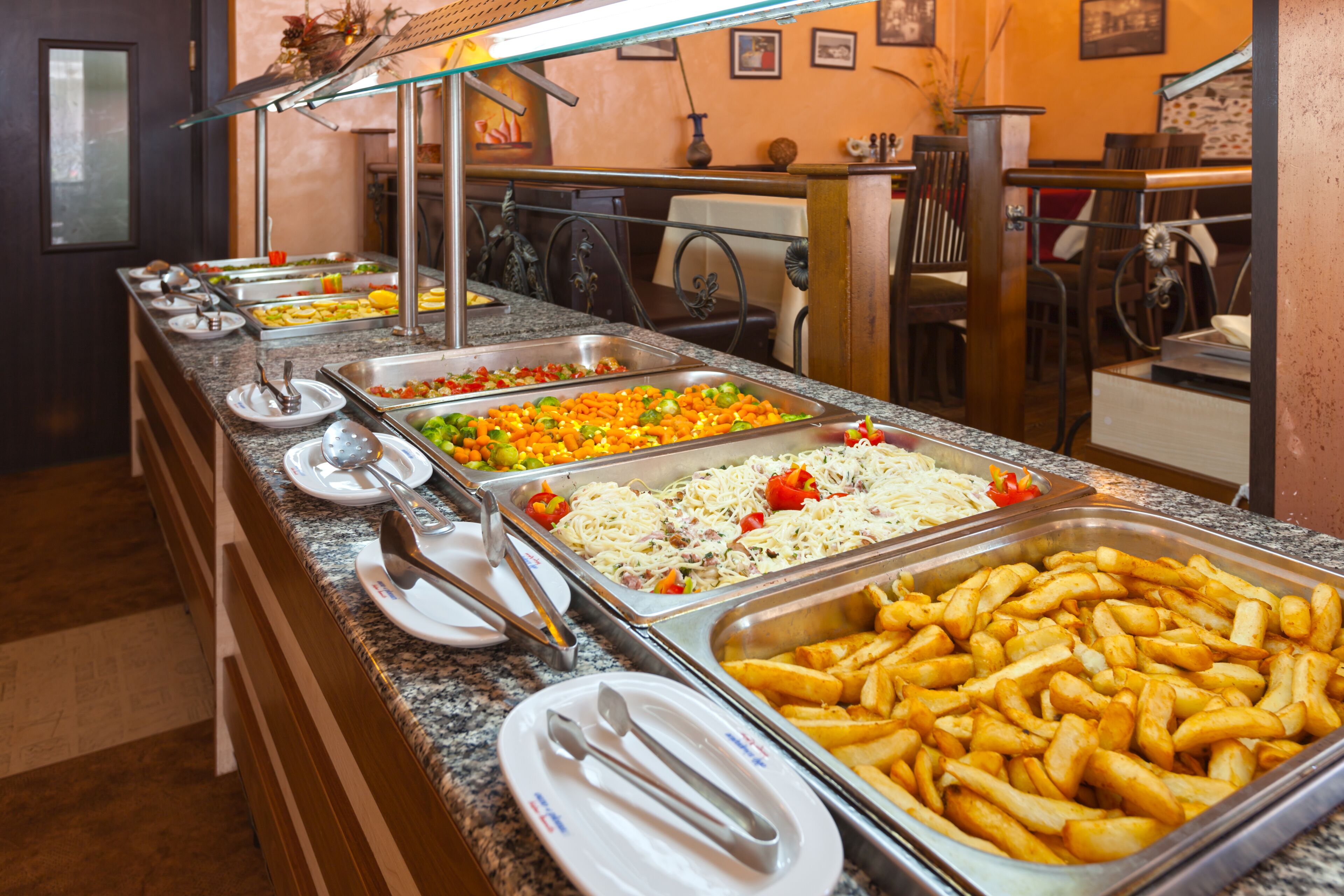 A buffet with various food options including pasta, vegetables, and French fries.