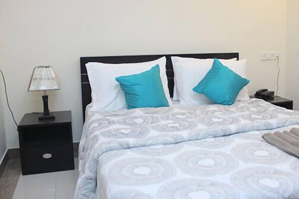 Una cama con colcha estampada, dos almohadas, una mesita de noche con lámpara y teléfono.